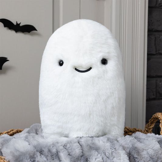 Plush white ghost with black eyes and smiling mouth, soft and fluffy texture, standing upright on a gray furry blanket.