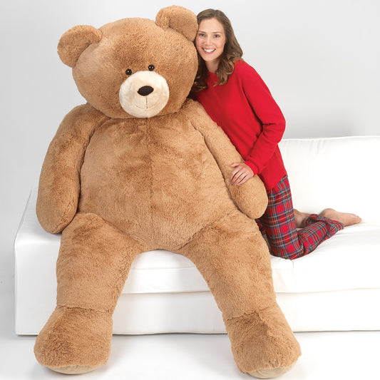 Woman in red shirt and plaid pants hugging a giant teddy bear on a couch.