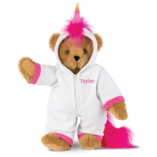 Honey-colored teddy bear wearing a white unicorn hoodie with pink accents and a bright pink tail and mane.